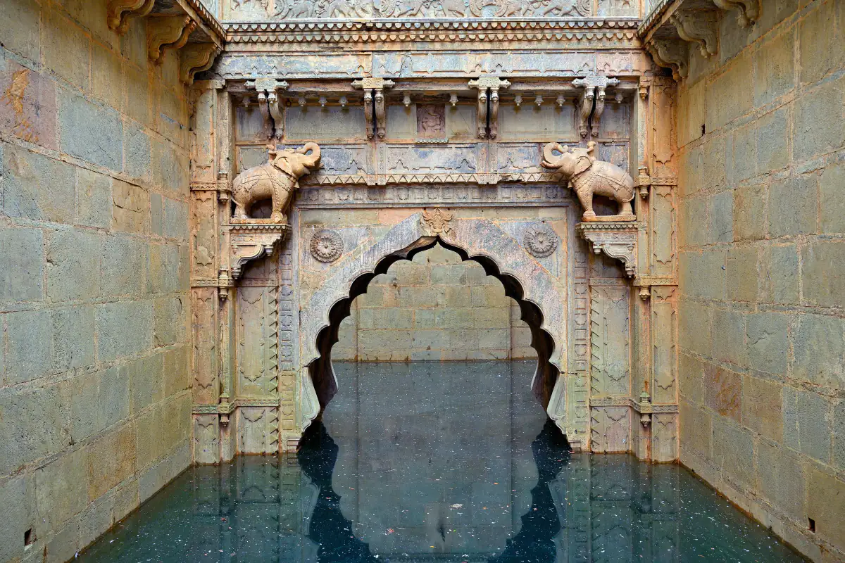 Carved arched gateway with elephant brackets over the water of Raniji ki Baori stepwell, Bundi